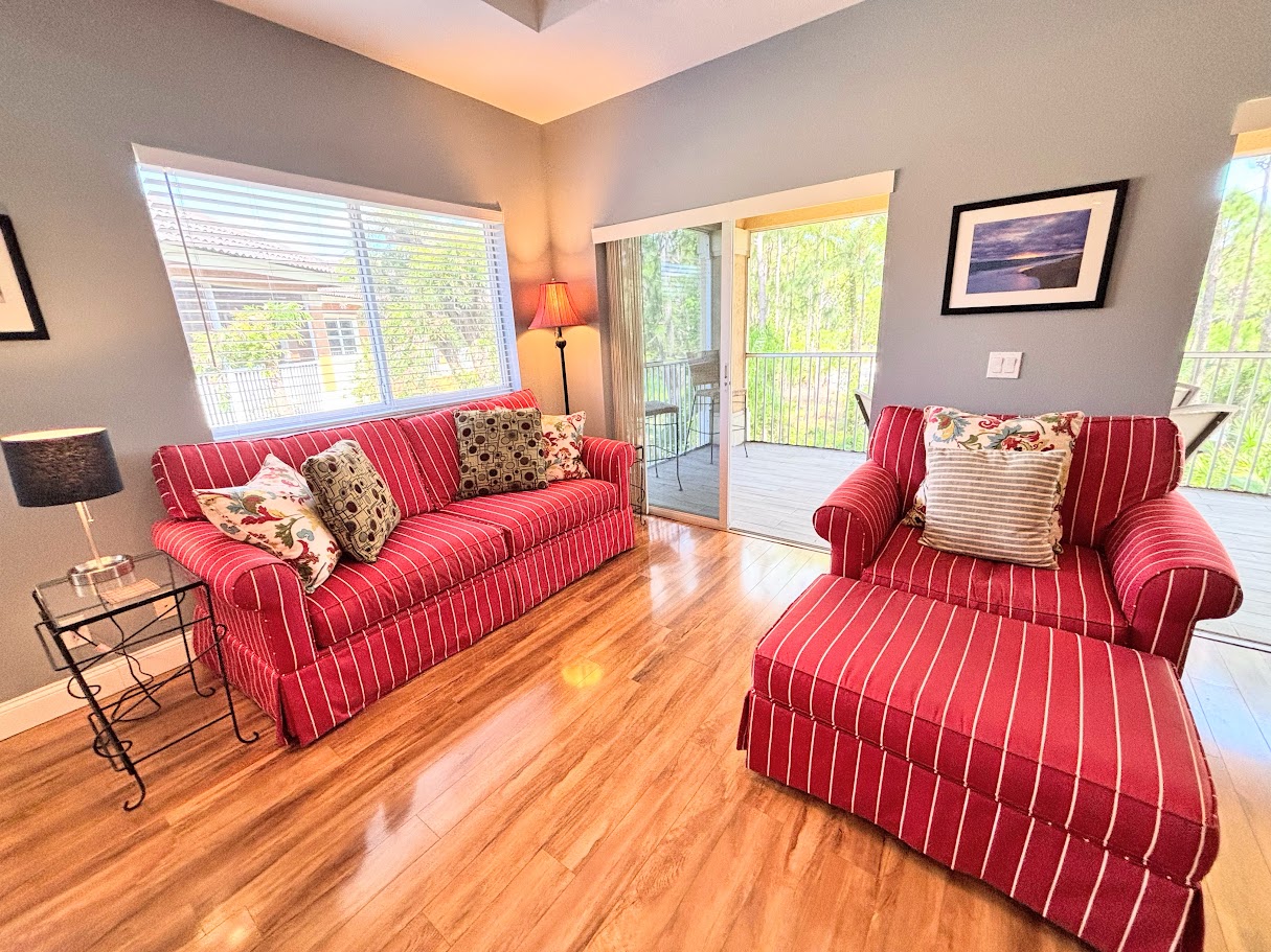 Comfortable living area featuring cozy red seating, wood-look flooring, and large windows overlooking the greenery.