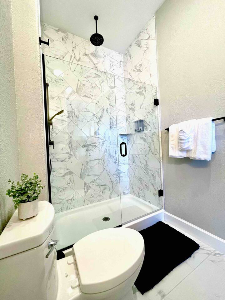 3rd Bedroom’s luxury bathroom, tiled to the ceiling, with overhead shower and hand wand, sink, and toilet. 