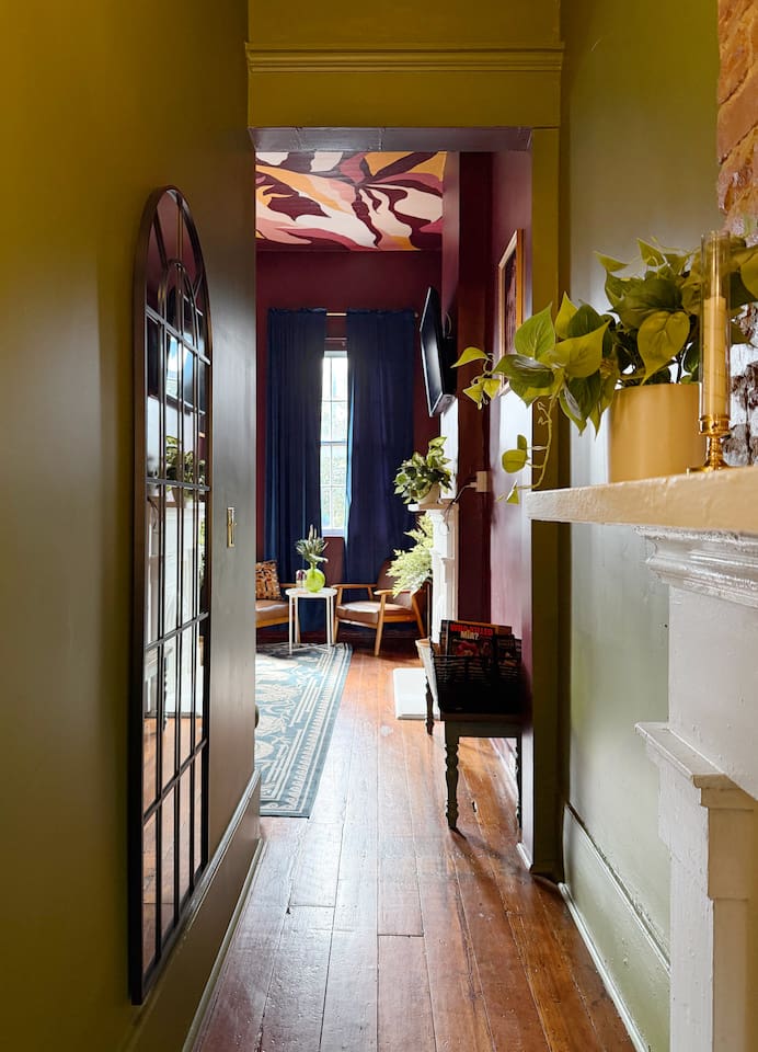 Historic hallway with original hardwood floors leading to the designer living room. This  charming New Orleans home blends classic architecture with bold modern interiors. 