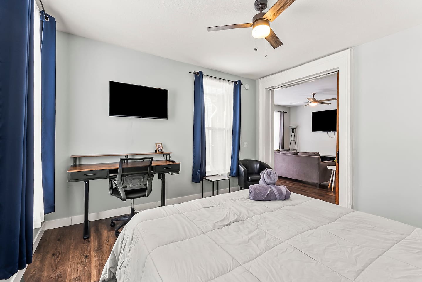 Dedicated workspace in the bedroom featuring a large desk, ergonomic chair, wall-mounted TV, and natural light—ideal for remote work.