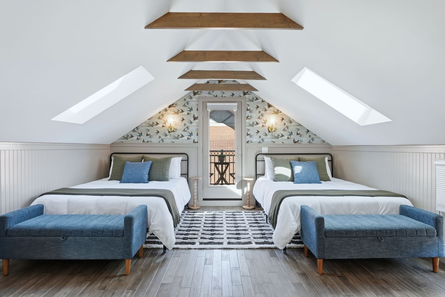 Spacious loft-style bedroom featuring two comfortable queen beds, vaulted ceilings with exposed wood beams, and stylish bird-pattern accent wall for a unique, cozy retreat.