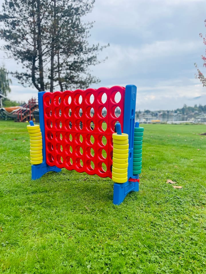 A giant Connect 4 game stands ready in the spacious backyard, offering playful fun for guests of all ages. The open lawn and nearby lake create a relaxed, inviting setting for outdoor games and gatherings.