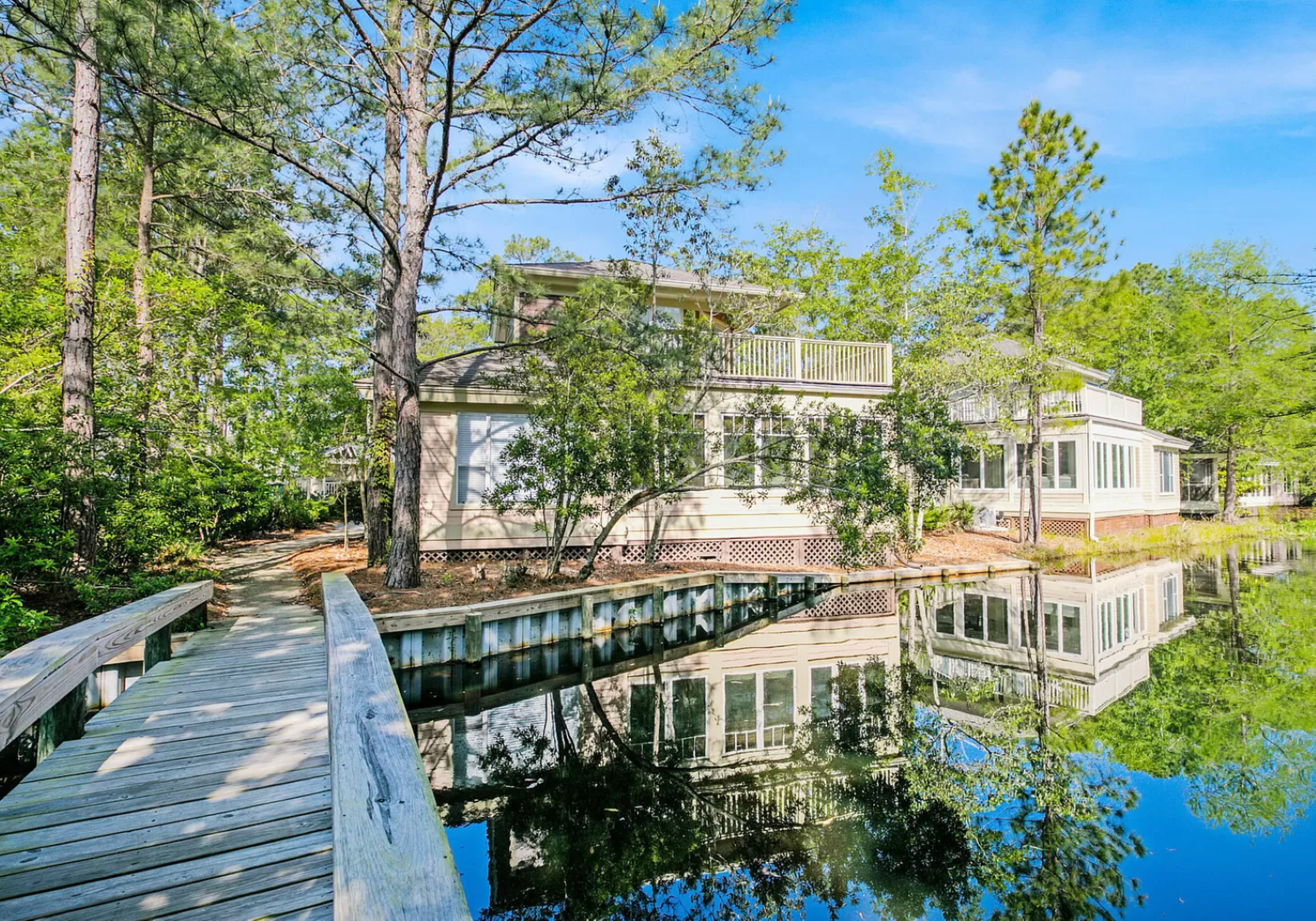 Tranquil water-side retreat at Bayside Bliss—reflections on a peaceful canal, framed by lush pines and a light-filled residence. 