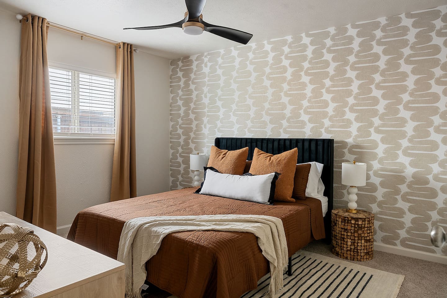 Enjoy a peaceful sleep in this stylishly furnished bedroom with chic wall coverings, comfortable furnishings, and a ceiling fan for extra comfort.