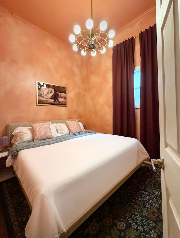 Sink into the plush king bed as the dramatic curtains draw and the ceiling fan hums. Soft light, serious comfort — the peach bedroom is your boutique hotel moment in the heart of NOLA.