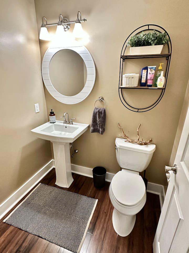 This classic powder room features a white pedestal sink and dark wood-style flooring. The neutral walls and simple patterned rug create a clean, inviting space for guests.