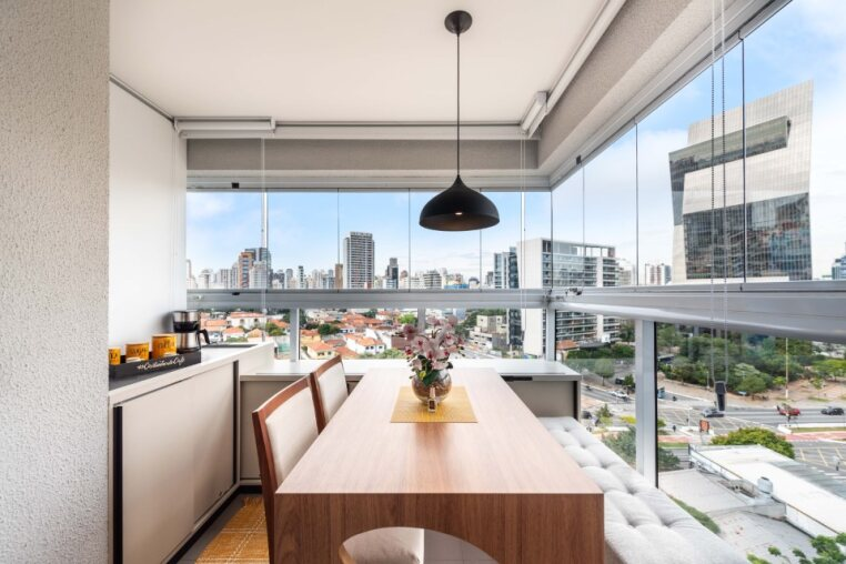 Varanda envidraçada com vista para a Faria Lima, mesa para 4 pessoas e cantinho do café — perfeita para refeições com skyline de São Paulo.