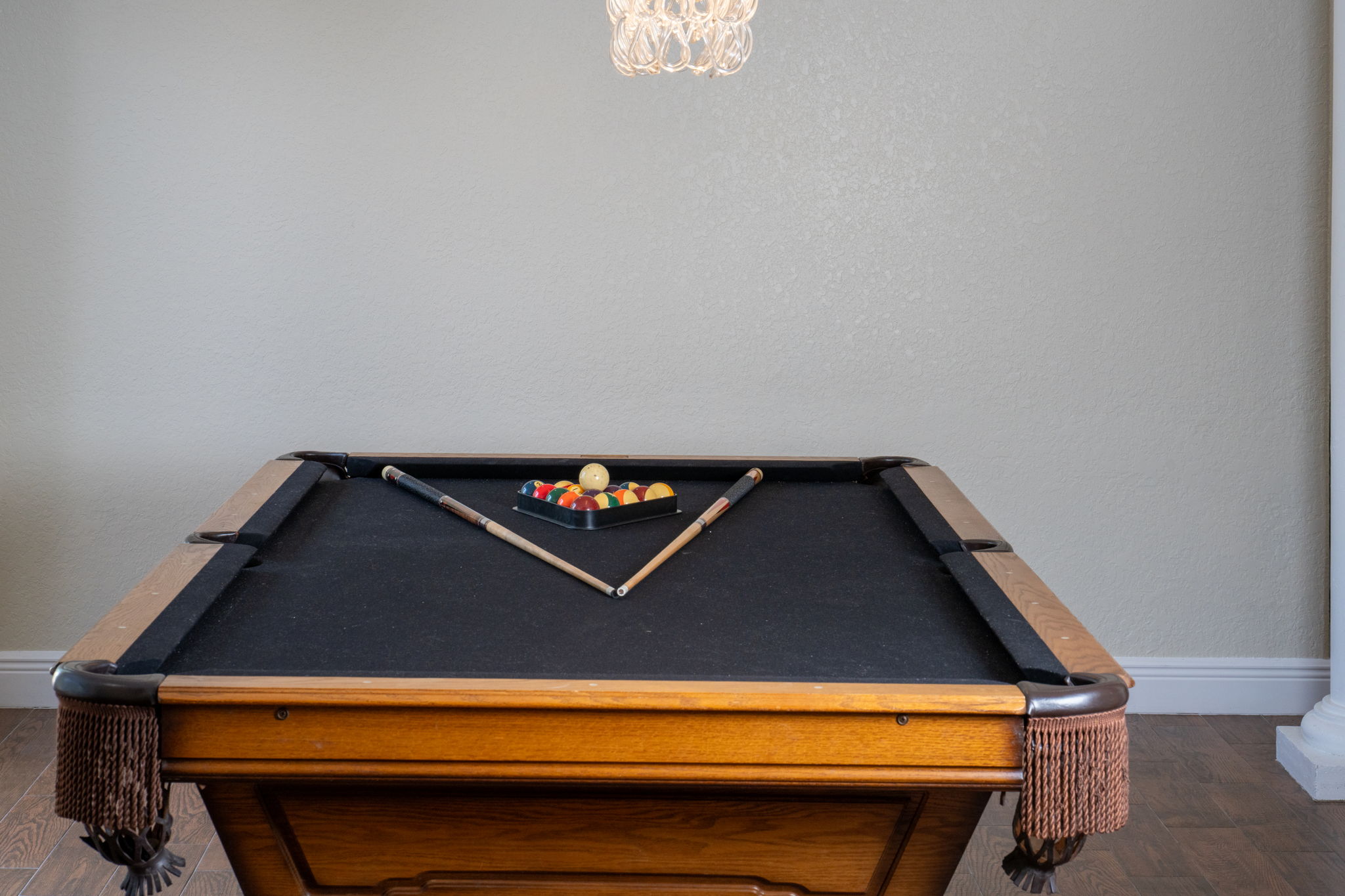 A bright and airy game room featuring a premium billiards table and sliding doors that lead to a patio with tropical landscaping and water views.