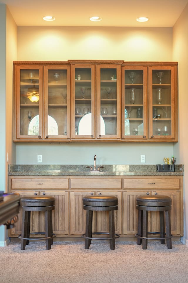 Built-in wet bar with granite countertop, glass-front cabinets, and bar seating—ideal for post-game drinks.