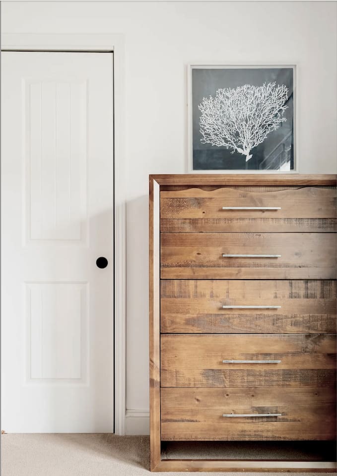 This close-up features a tall dresser made of rustic wood with horizontal silver-tone handles. It sits next to a generous sized closet.