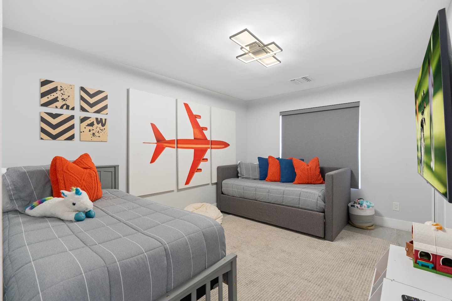 This bright and playful bedroom showcases an aviation theme with a bold airplane mural, a cozy single bed, and cheerful orange and grey accents — perfect for younger guests or the young at heart.