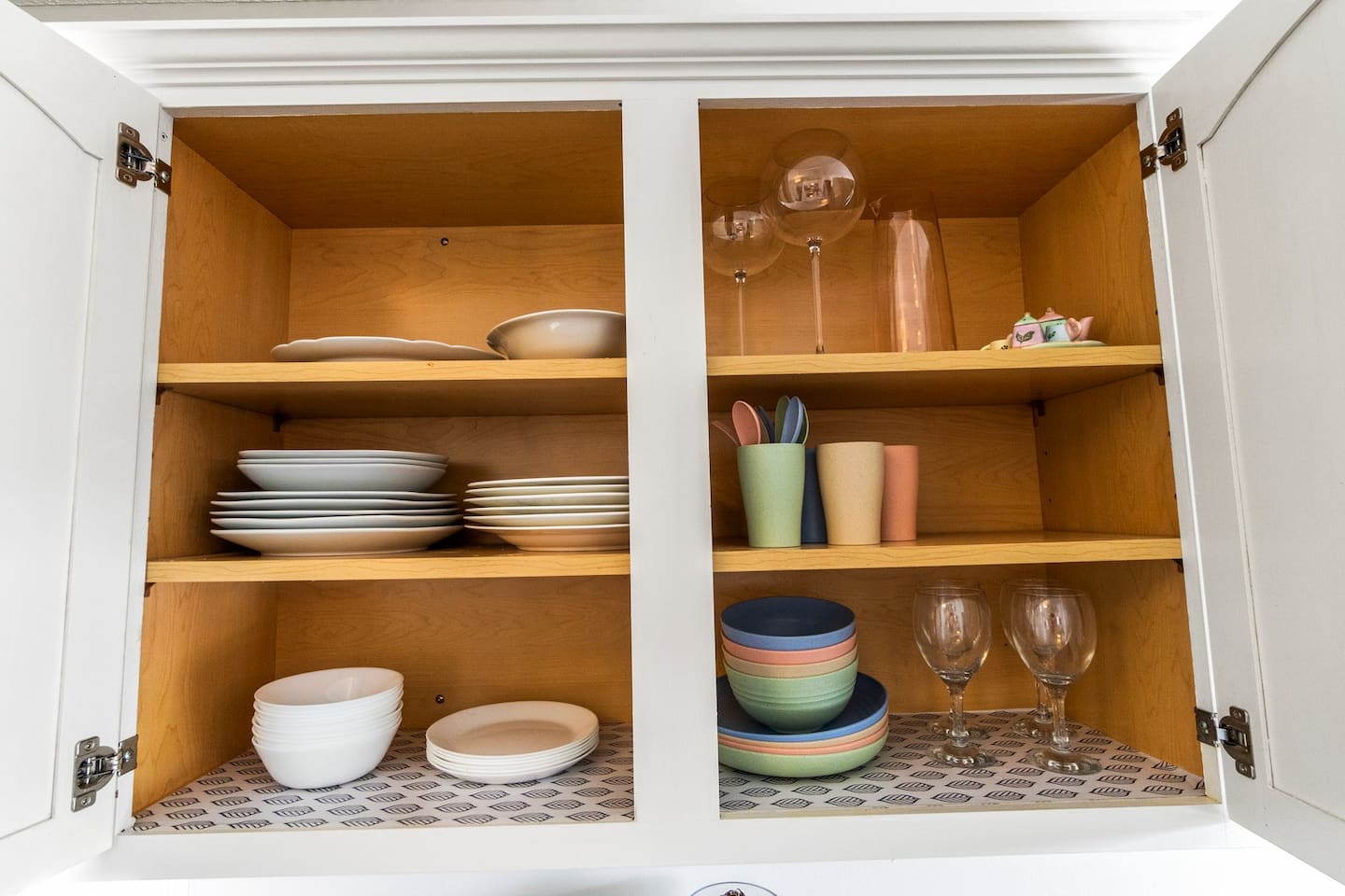 A well-stocked cabinet featuring elegant white dinnerware, colorful bowls, wine glasses, and charming cups—plus dedicated kid-friendly dinnerware to ensure even the littlest guests feel at home.