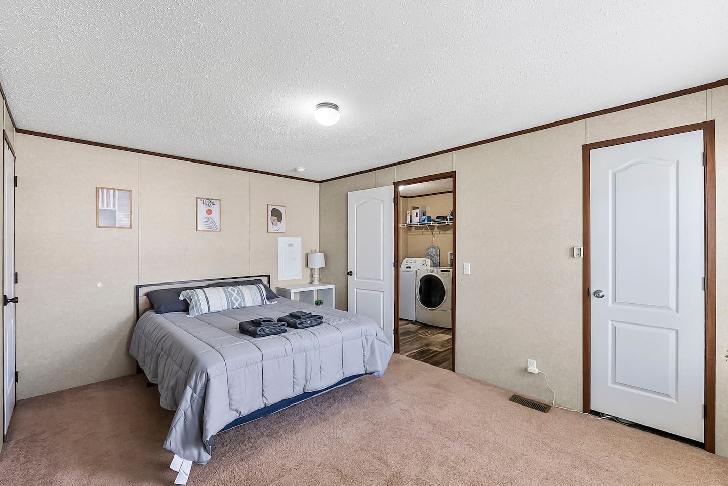 Spacious master bedroom with a comfortable queen bed, soft carpeting, and easy access to the laundry area for added convenience.
