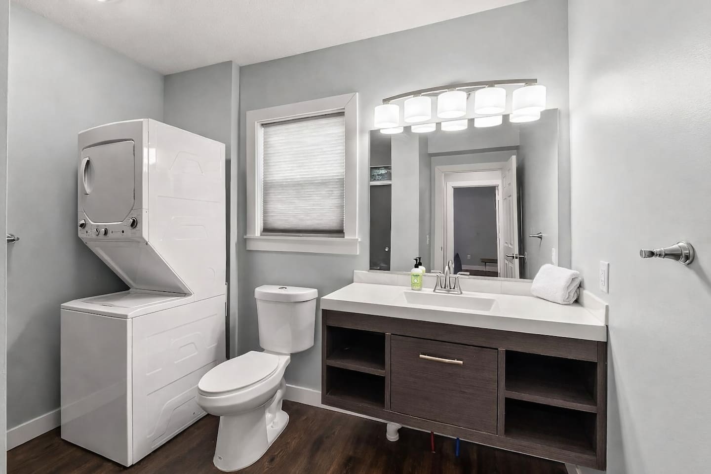 Modern full bathroom featuring a sleek vanity, bright lighting, toilet, and in-unit washer and dryer for added convenience.