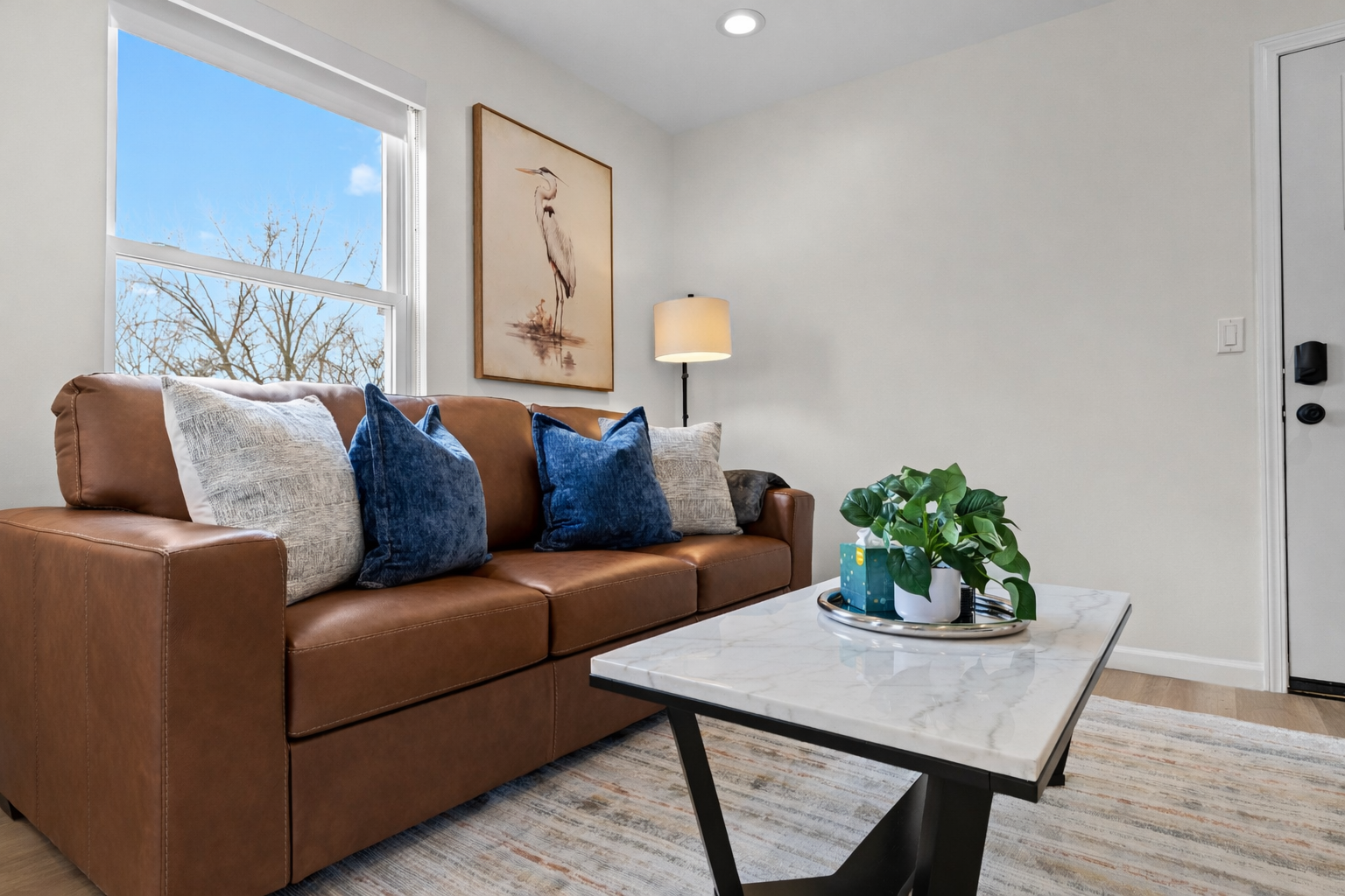 Sun-filled living room with a plush leather sofa, stylish décor, and calming artwork—an inviting spot to relax, recharge, and enjoy the natural light.