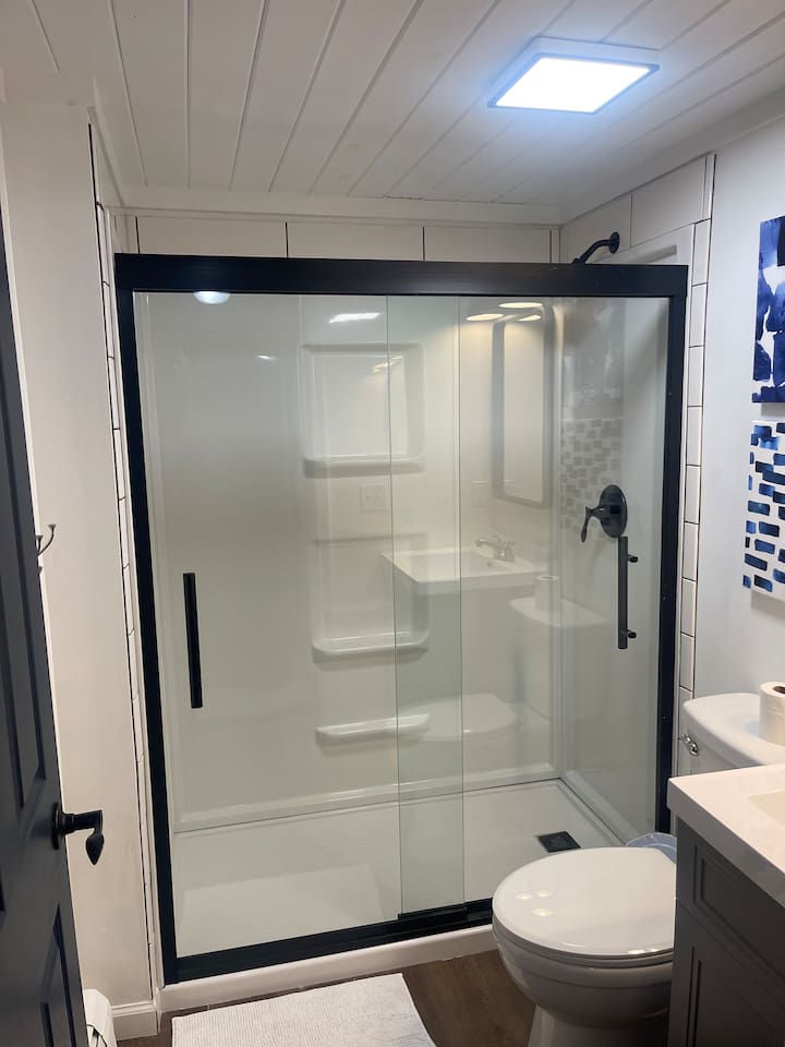 This updated bathroom features a spacious walk-in shower with sleek glass doors and matte black fixtures. Clean white tile, warm wood flooring, and modern lighting create a fresh, spa-like feel—perfect for relaxing during your short-term stay.