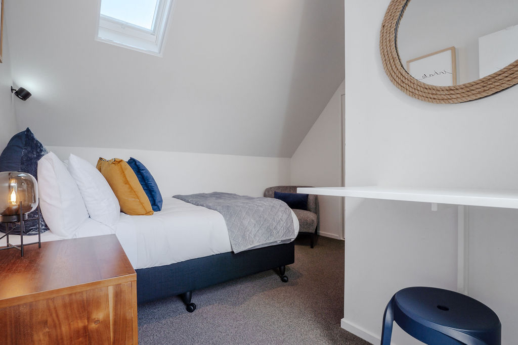 A cosy upper-level bedroom at Fernhill Mountain Escape, with skylight light, warm bedside detail and a quiet chair tucked near the bed.