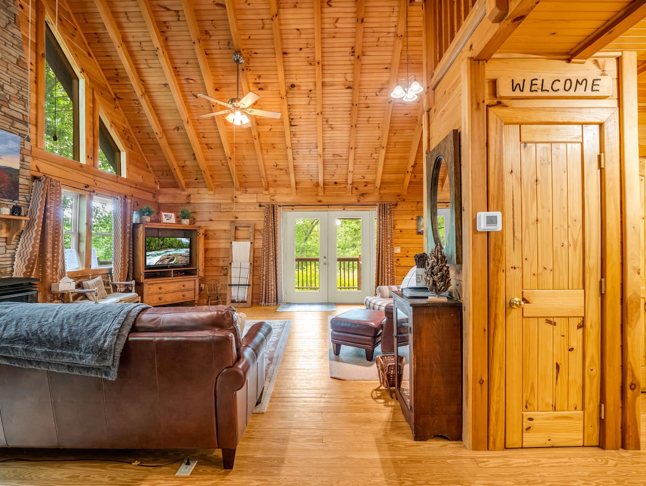 Spacious main living room area with soaring wood ceilings, comfortable seating, and deck access with overlooking trees