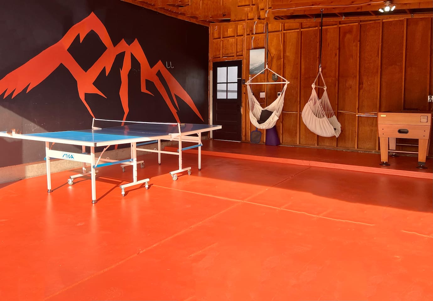 Converted garage for games with ping pong, foosball, hanging chairs and mountain mural for rain or shine entertainment. 