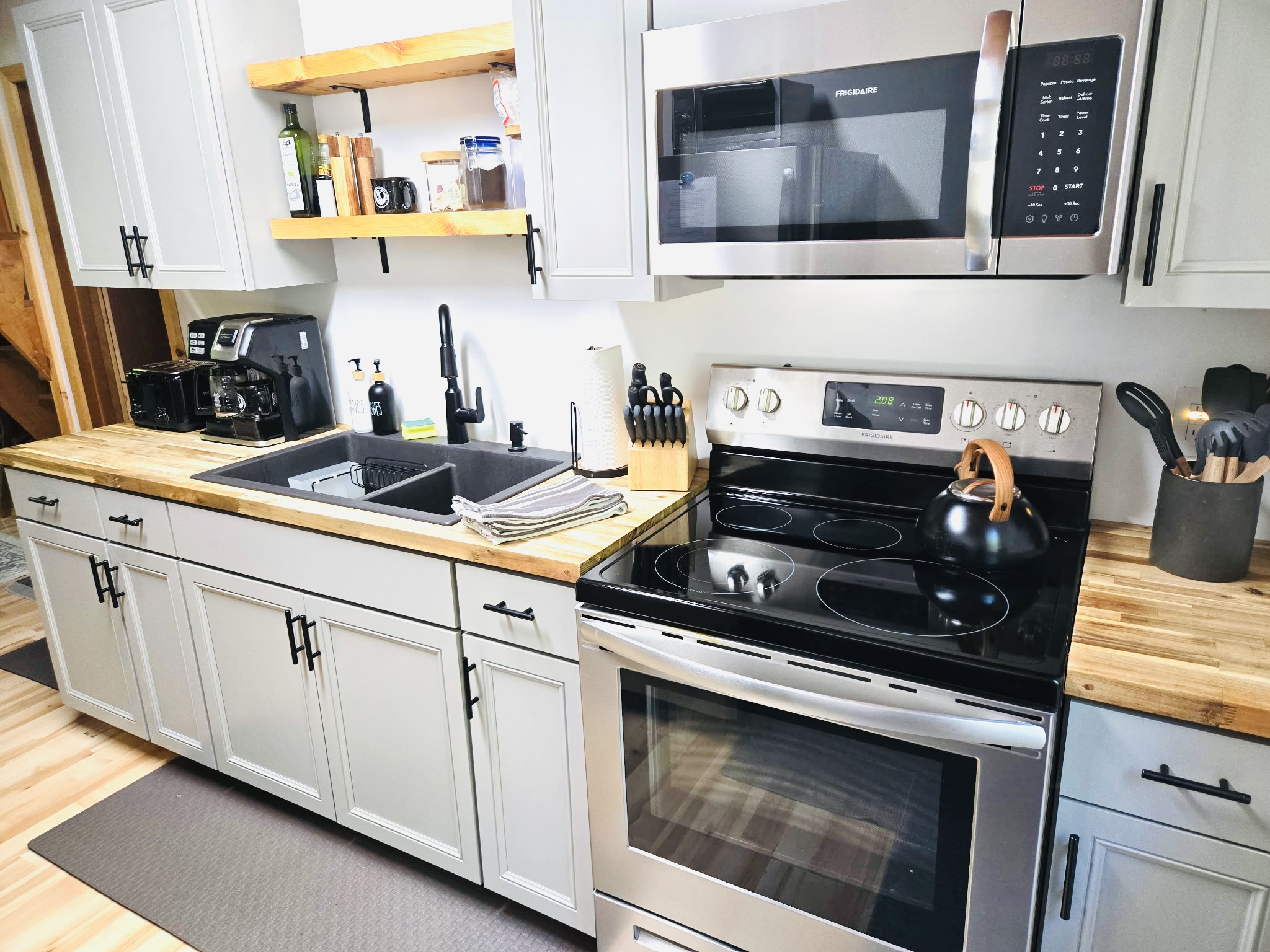 Galley kitchen with stove, microwave, refrigerator, toaster, dual coffee maker.