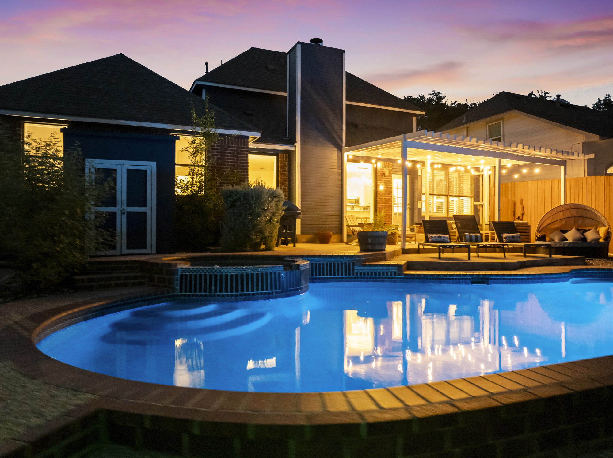 Stunning backyard retreat featuring a sparkling pool, spa, and a covered patio with cozy seating and string lights. Perfect for relaxing evenings or outdoor entertaining.