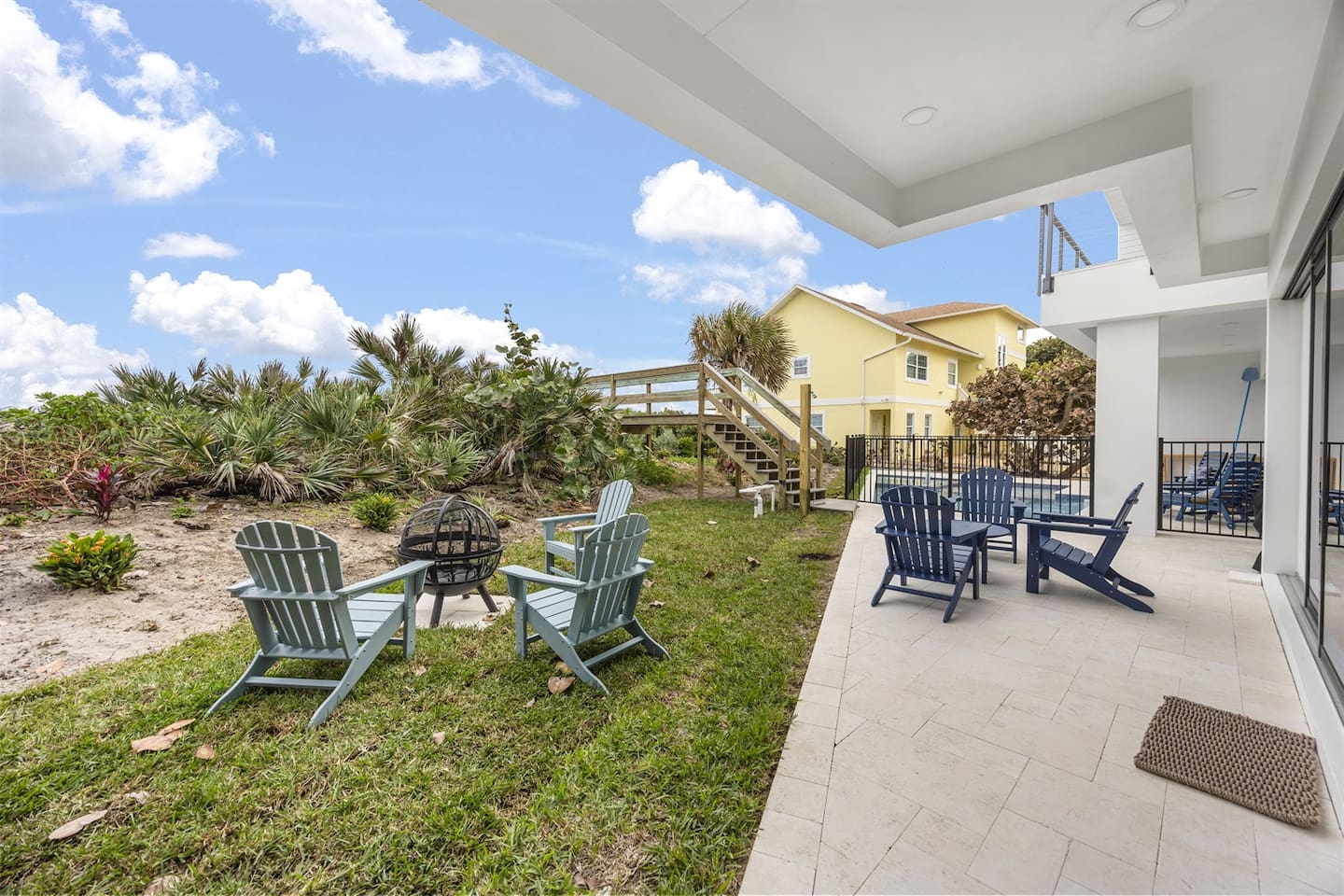 Enjoy the outdoors with tables and chairs, surrounded by lush greenery, a bridge leading to the ocean, and stunning neighborhood views, offering the perfect setting for relaxation and sightseeing in a picturesque location
