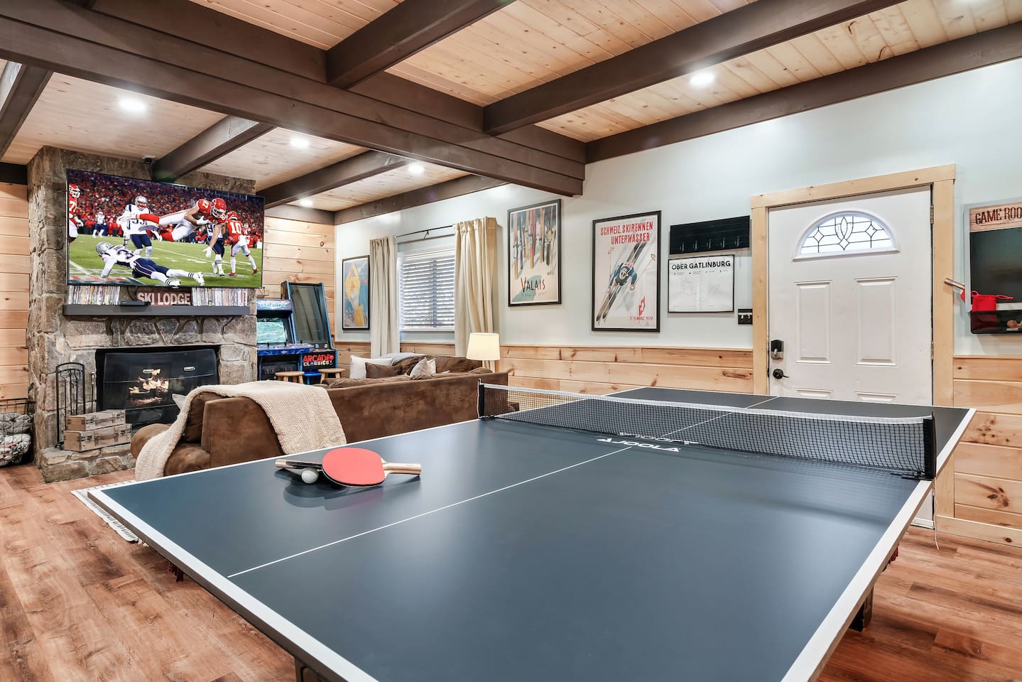 The game room on the lower level features another living space with 75" smart TV, ping-pong table topper, a pool table (remove ping pong top), mini fridge, cornhole boards, arcade games, and a pull-out sofa bed. Plus a full bathroom.