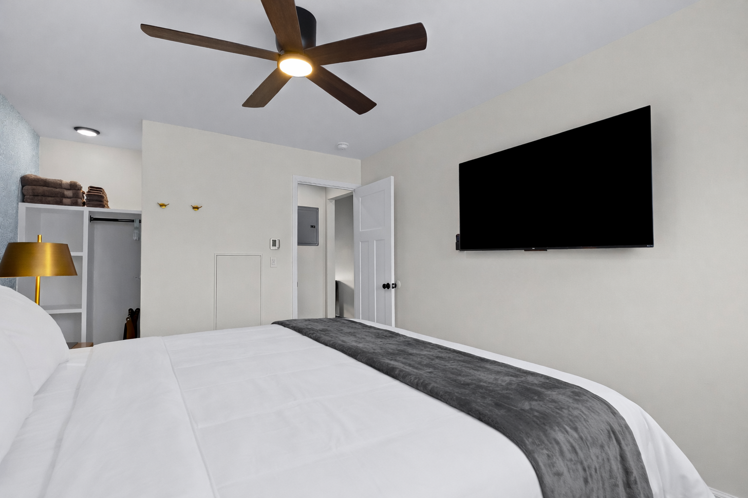 Kick back in this cozy bedroom with a wall-mounted smart TV, ceiling fan, and plush bedding—perfect for winding down and enjoying a quiet night in.
