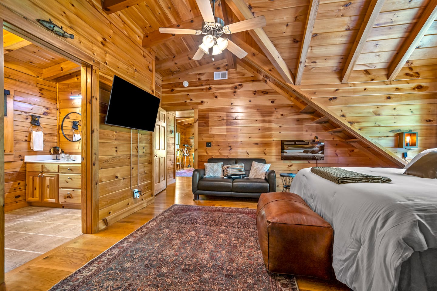Spacious master bedroom featuring a king-sized bed, vaulted ceilings, a cozy seating area, mounted TV, and an ensuite bathroom.