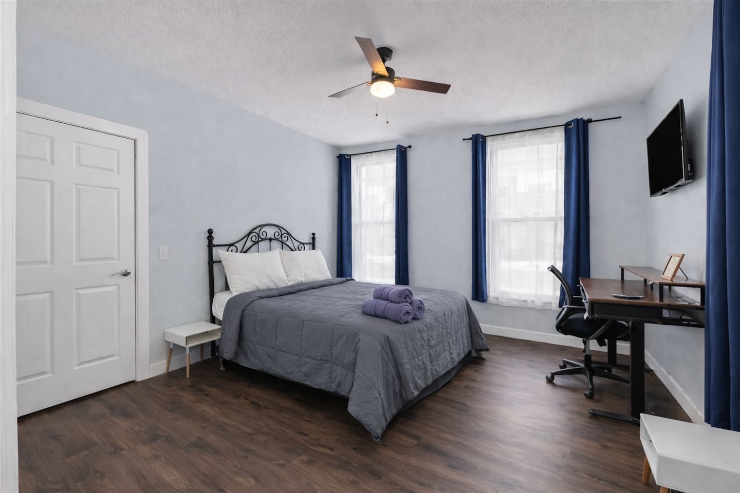 Spacious primary bedroom featuring a comfortable queen-size bed, high ceilings, and warm natural light & work space area.