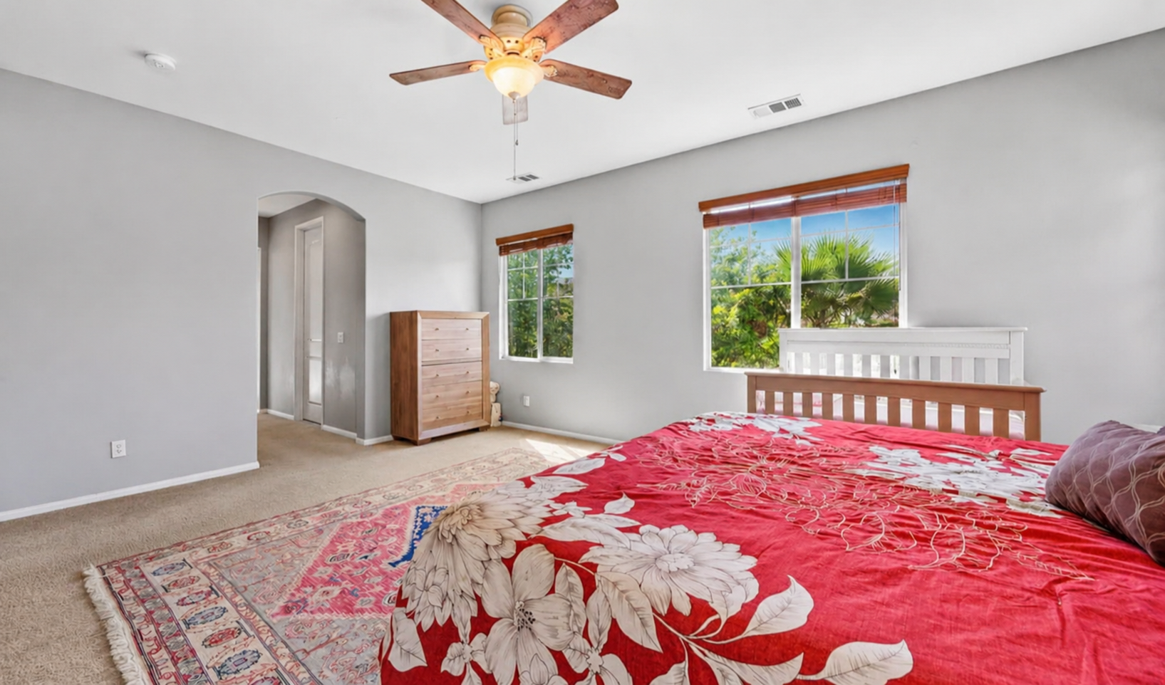 Primary bedroom with soft bedding, ceiling fan, dresser storage, and peaceful window views.