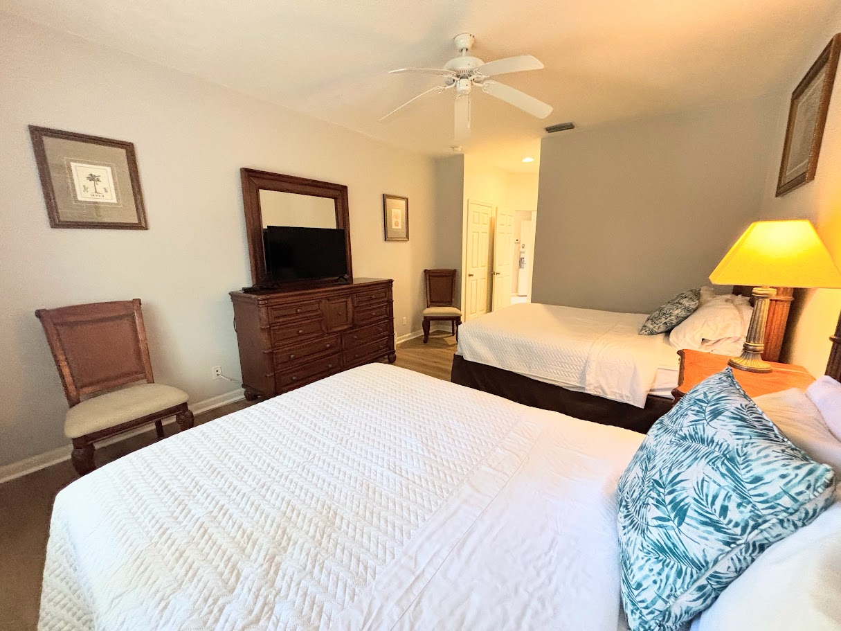 Spacious bedroom with two beds, dresser storage, ceiling fan, and a clean, relaxing layout.