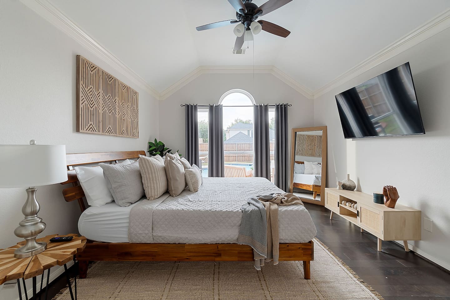 Rustic meets modern in this tranquil bedroom, with a grand bed, minimalist furnishings, and a sleek TV, all bathed in natural light.