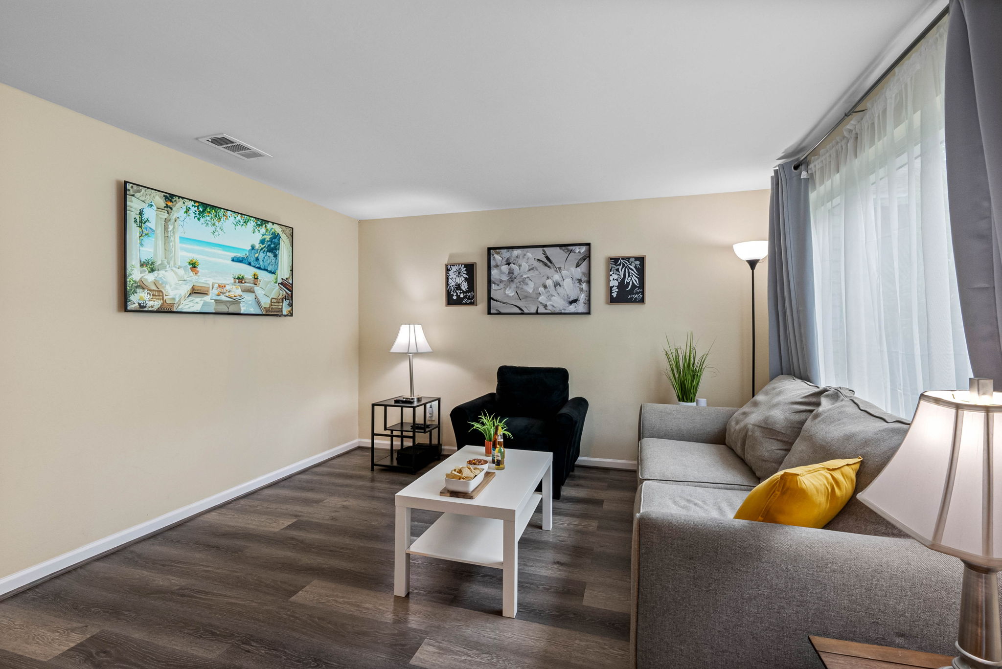 The room features a plush light gray sectional sofa with deep seating and a cheerful yellow accent pillow that adds a splash of warmth and personality.