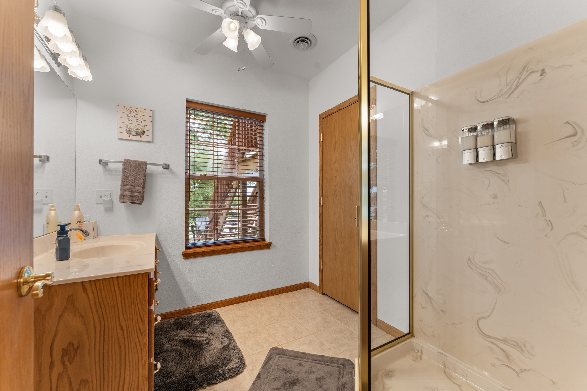 Lower-level full bathroom with oak vanity and walk-in shower. Marble-look shower walls and wall-mounted soap dispensers.