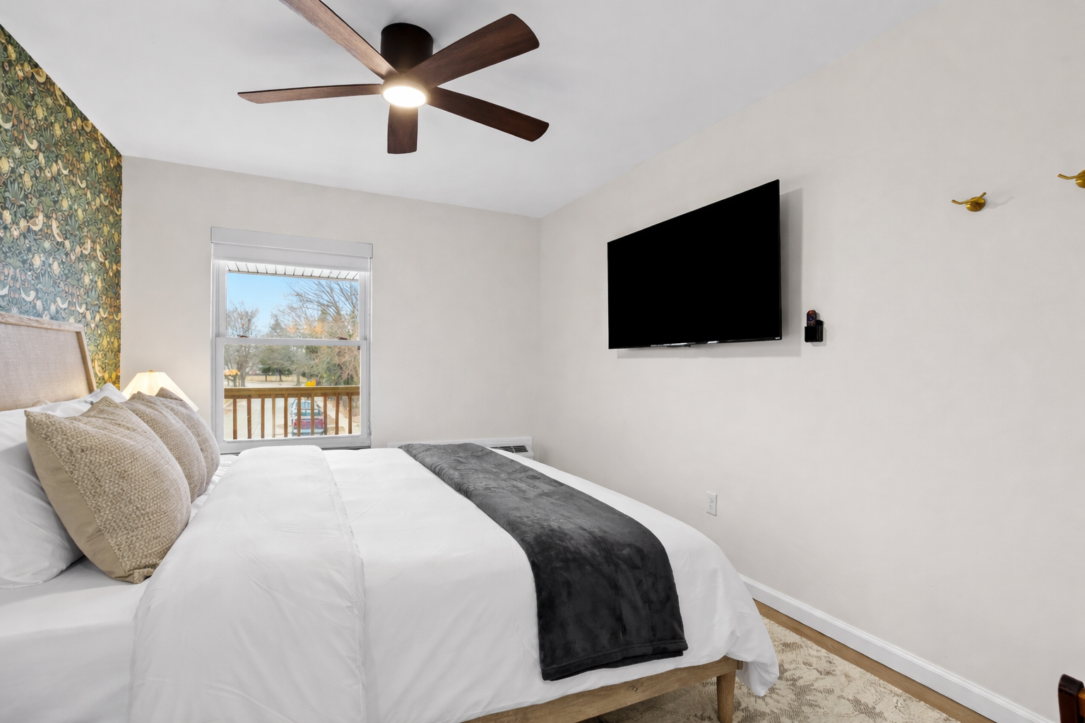 Bright, comfortable bedroom with a plush bed, smart TV, ceiling fan, and natural light—ideal for relaxing nights and easy mornings.