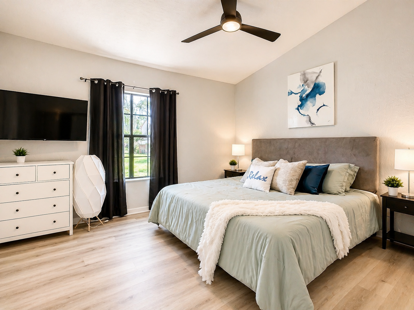 Comfortable bedroom featuring queen bed, large window with natural light, and ceiling fan for guest comfort.