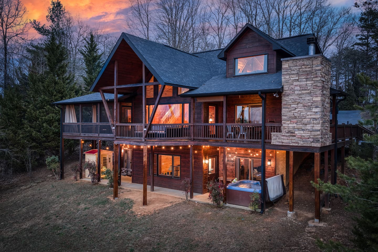 The back of the beautiful "Blessed Sunset" mountain retreat home overlooking the back yard! Stunning A-frame, wrap-around porch, screened-in patio, outdoor fireplace, outdoor dining table, sauna, hot tub, outdoor couch, and more!