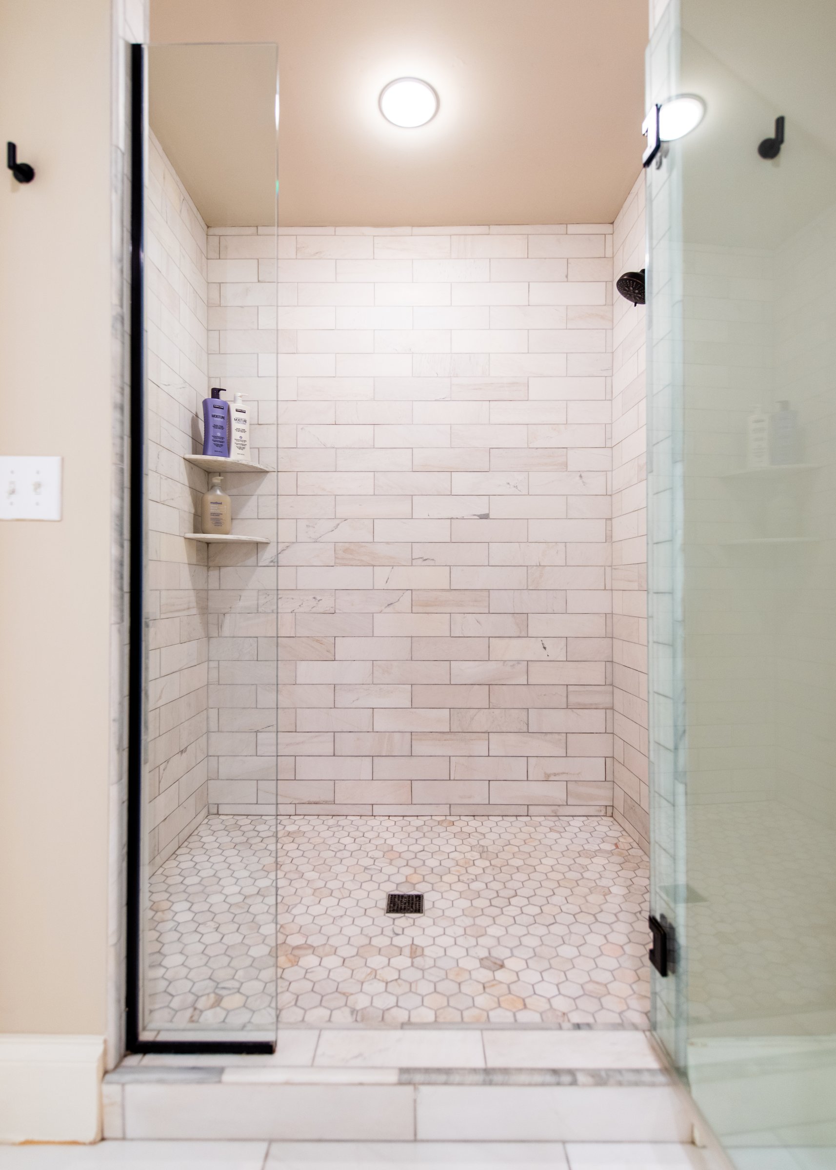 A glass-enclosed walk-in shower finished in marble subway tile.