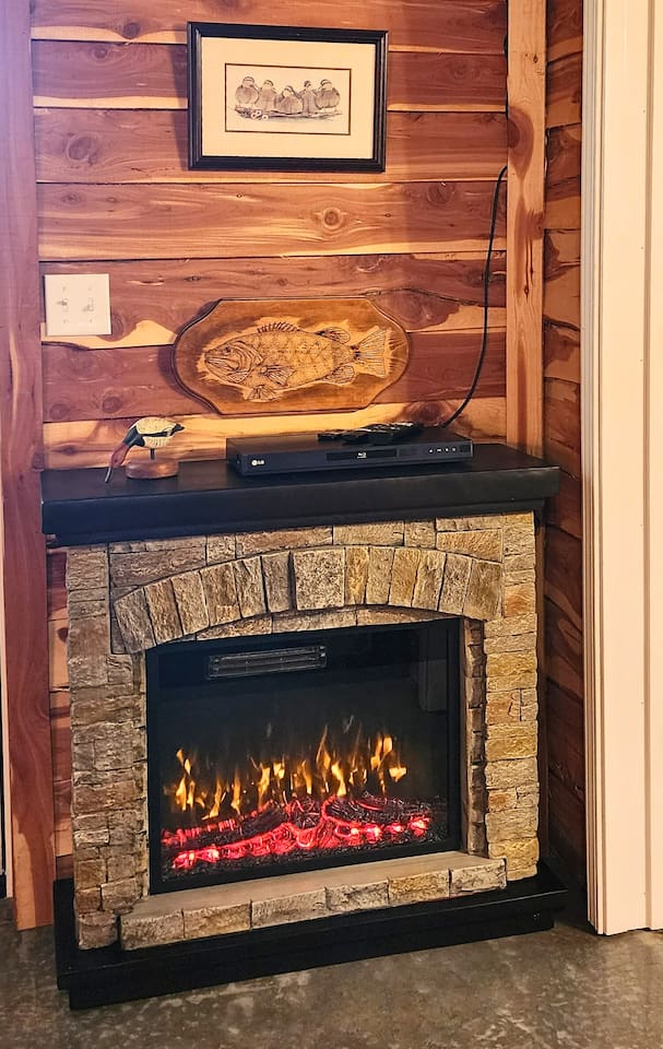 The lodge’s electric fireplace adds a warm, flickering glow and rustic charm to your stay. Framed by stacked stone and topped with fishing-themed decor, it’s the perfect spot to unwind after a day of hiking, fishing, or simply relaxing in nature.