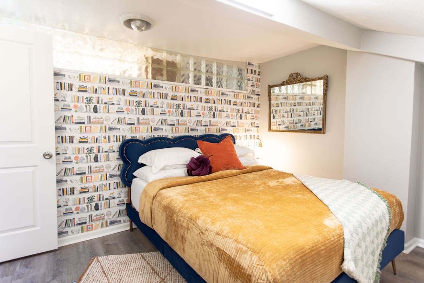 Indulge in ultimate comfort in this stylish bedroom, featuring a plush queen bed adorned with luxury linens. The unique bookshelf wallpaper adds a touch of character and sophistication, creating a cozy yet chic retreat. Enjoy the soft glow of the bed