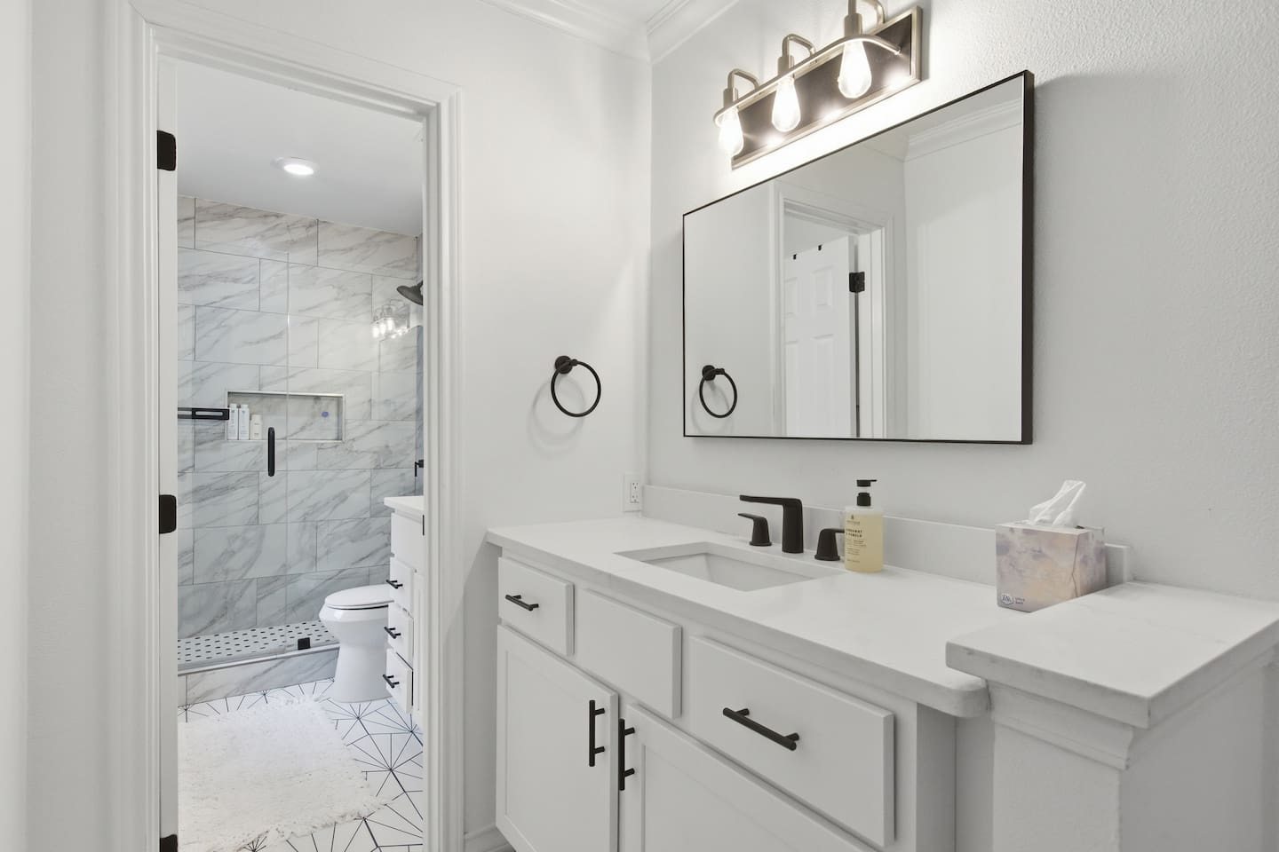 Modern full bathroom with rain shower, double vanity, large mirror, bright lighting, and fresh towels for guest comfort.