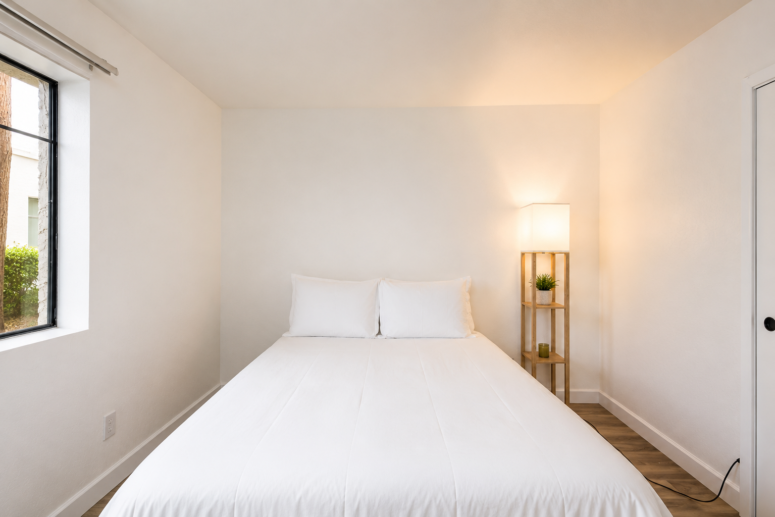 Simple queen bedroom with fresh white bedding, wood-look floors, closet space, and a floor lamp by the bed.