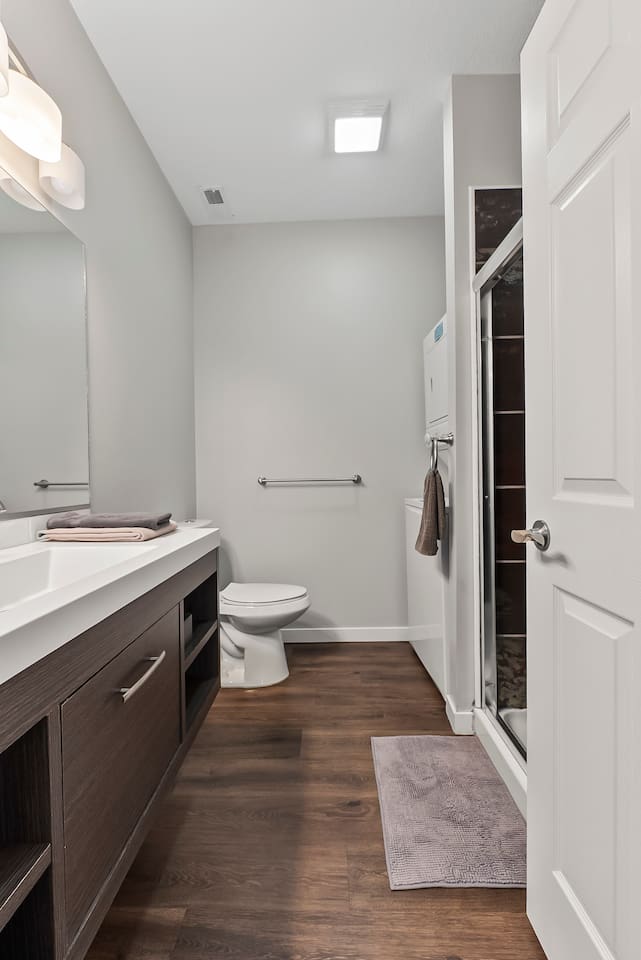 Spacious bathroom with sleek flooring, walk-in shower, and convenient in-unit laundry.