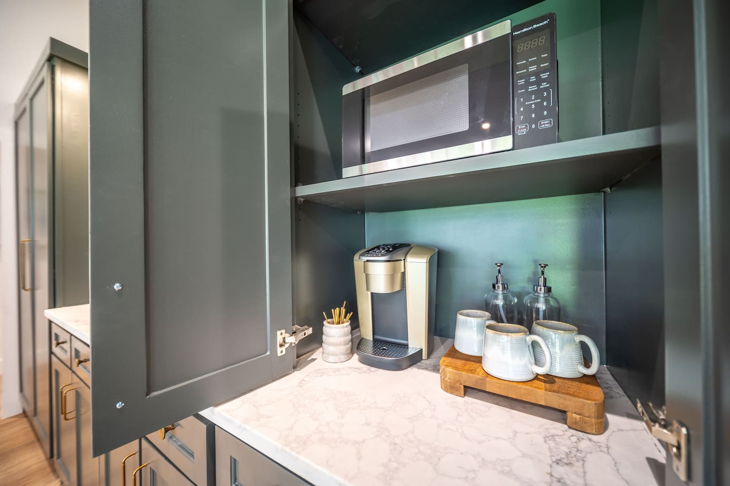Built-in coffee station with microwave and single-serve coffee maker, stocked with coffee, flavored syrups, creamer, sweeteners, and coffee bar essentials for an easy, elevated morning routine.