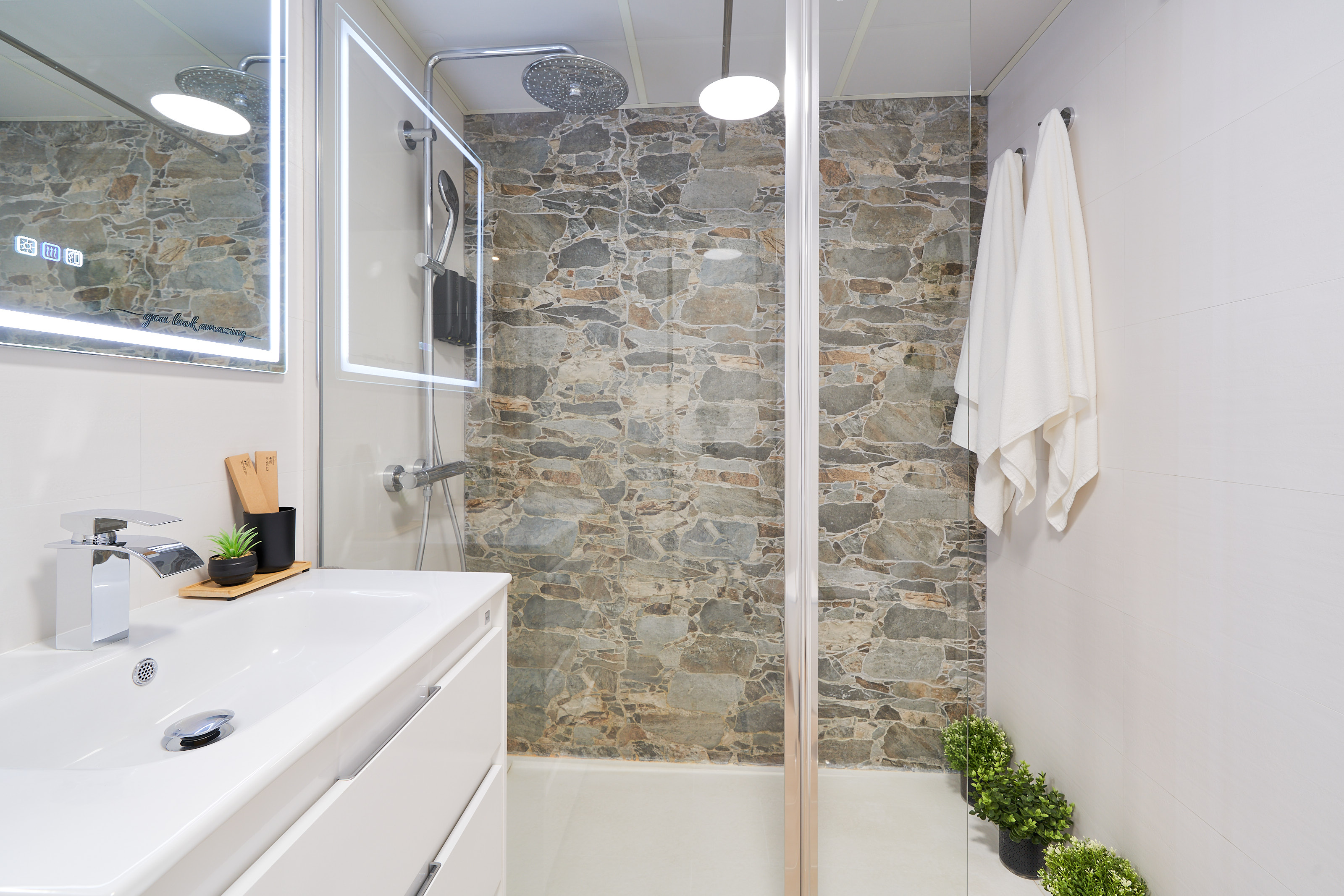 Modern bathroom with walk-in rain shower, stone accent wall, LED mirror, and fresh spa-like touches for your comfort.