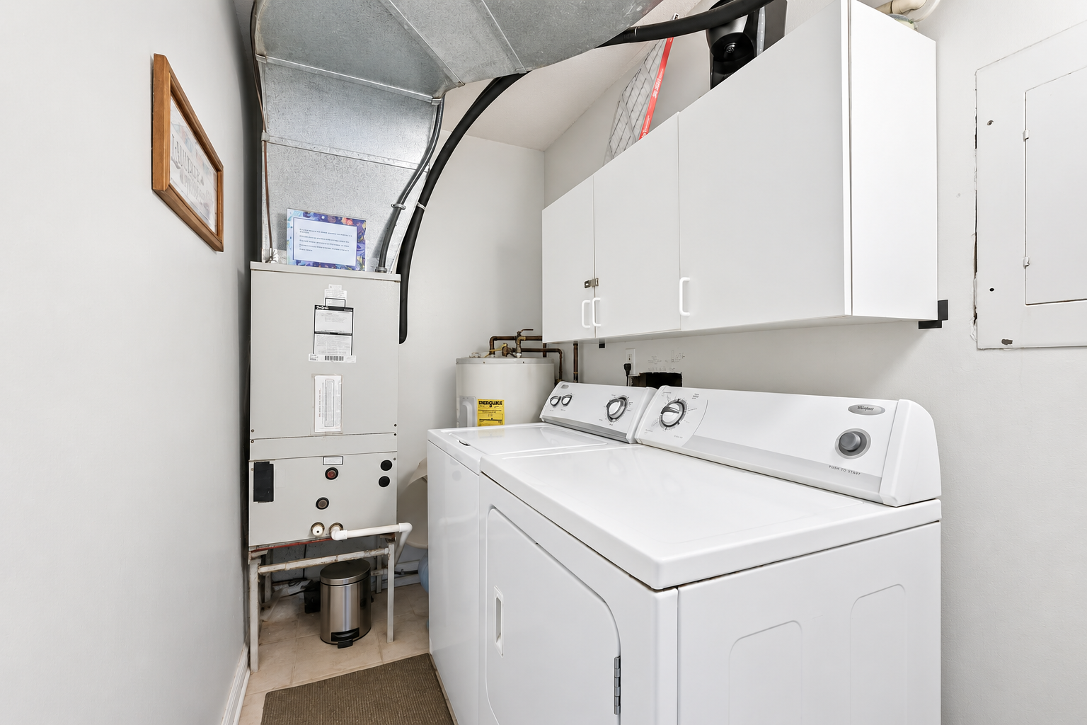 In-unit laundry room with washer, dryer, overhead cabinets, and HVAC equipment tucked away from the main living areas.
