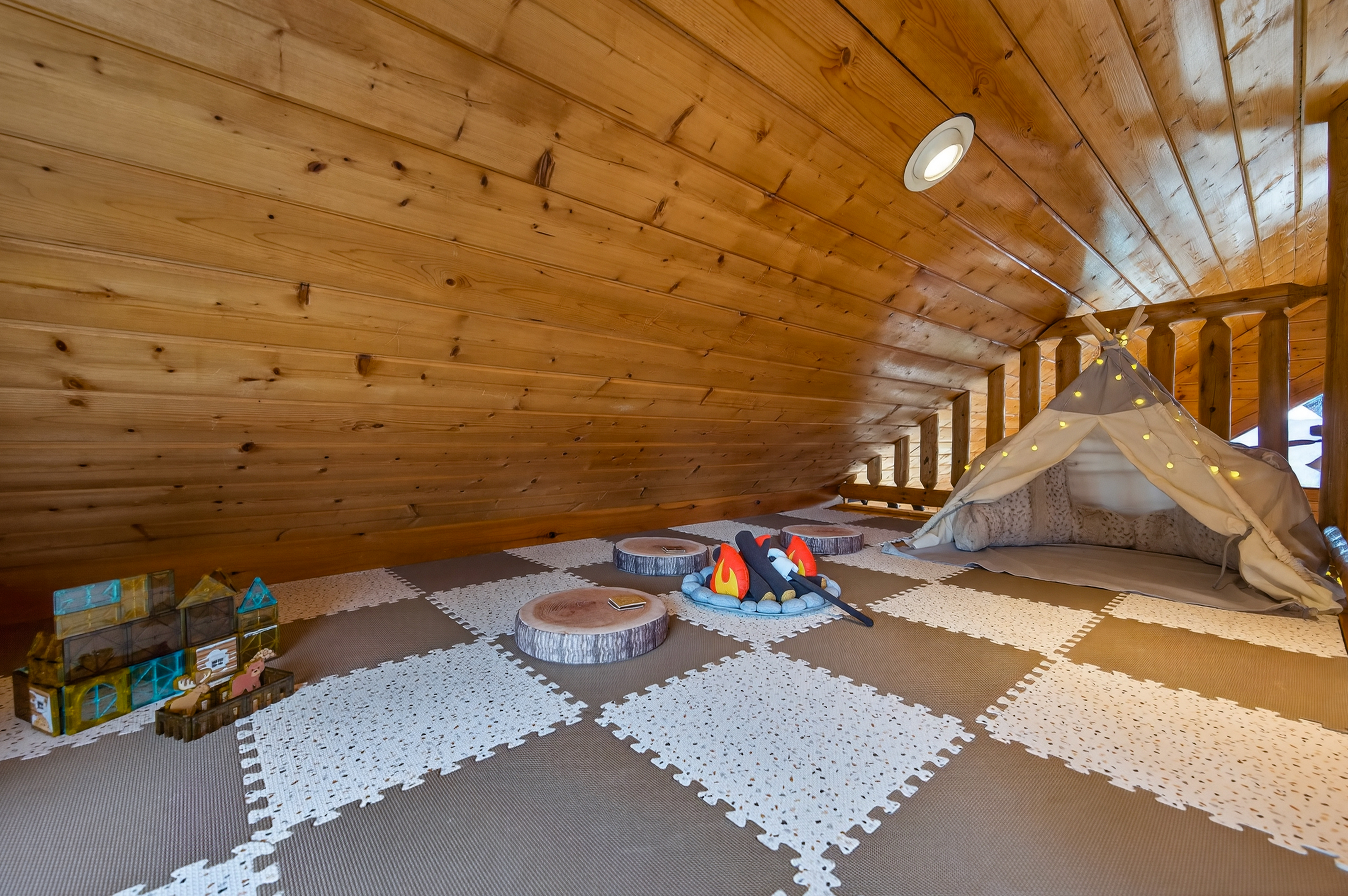 The kids' secret loft hideaway — tucked above the upper bedroom with a teepee, fairy lights, pretend s'mores campfire, wood slice seats, and cabin-themed building tiles. They'll disappear up here for hours.