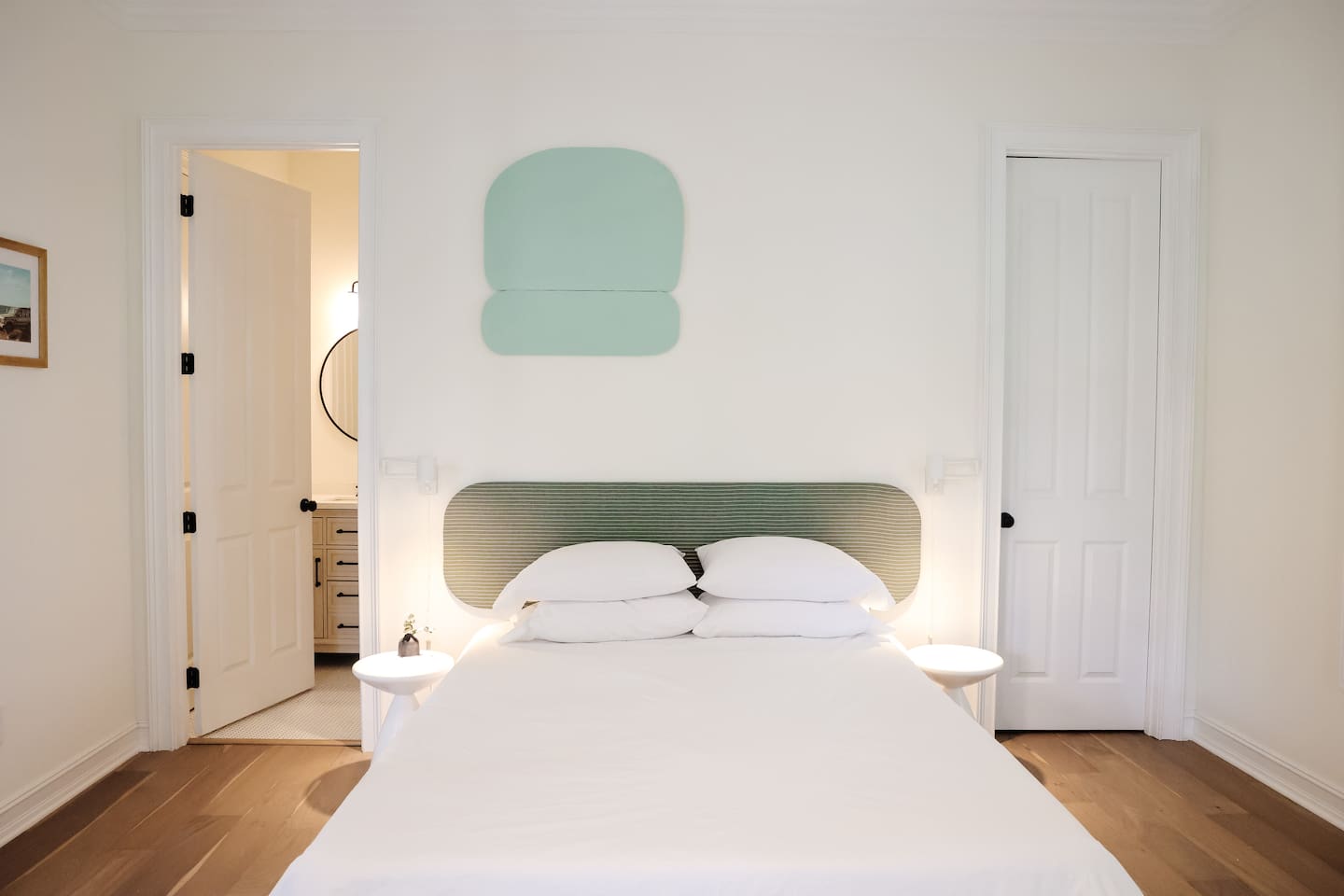 The downstairs bedroom is an airy oasis. Featuring custom art and headboard - the spacious room has a queen size bed, a walk-in closet, a desk for work-from-home, smart TV and direct access to a full bathroom.