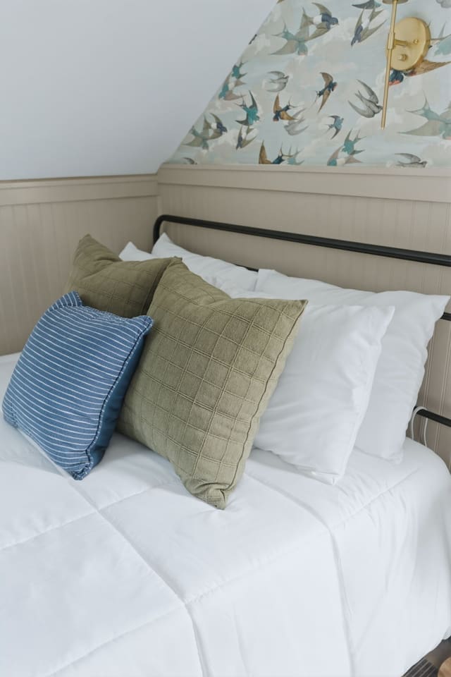Detailed view of the bed featuring comfortable pillows, crisp white linens, and charming bird-pattern accent wall.